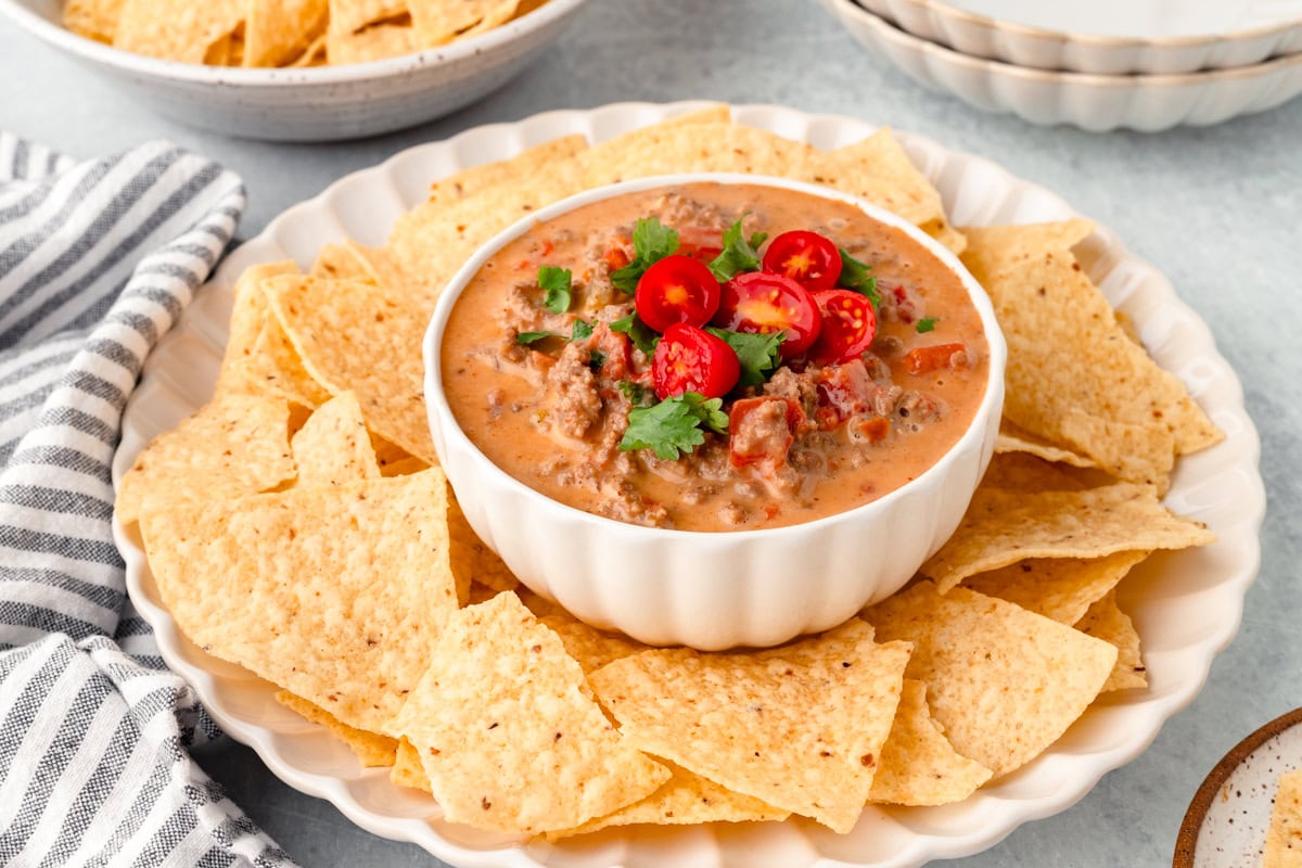 Creamy taco meat dip with tomatoes and cilantro on tortilla chips, perfect for parties.