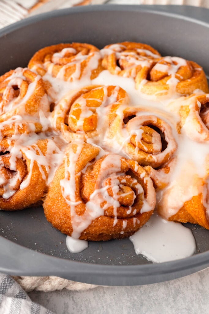 Cinnamon rolls with icing drizzled on top in a gray baking dish.