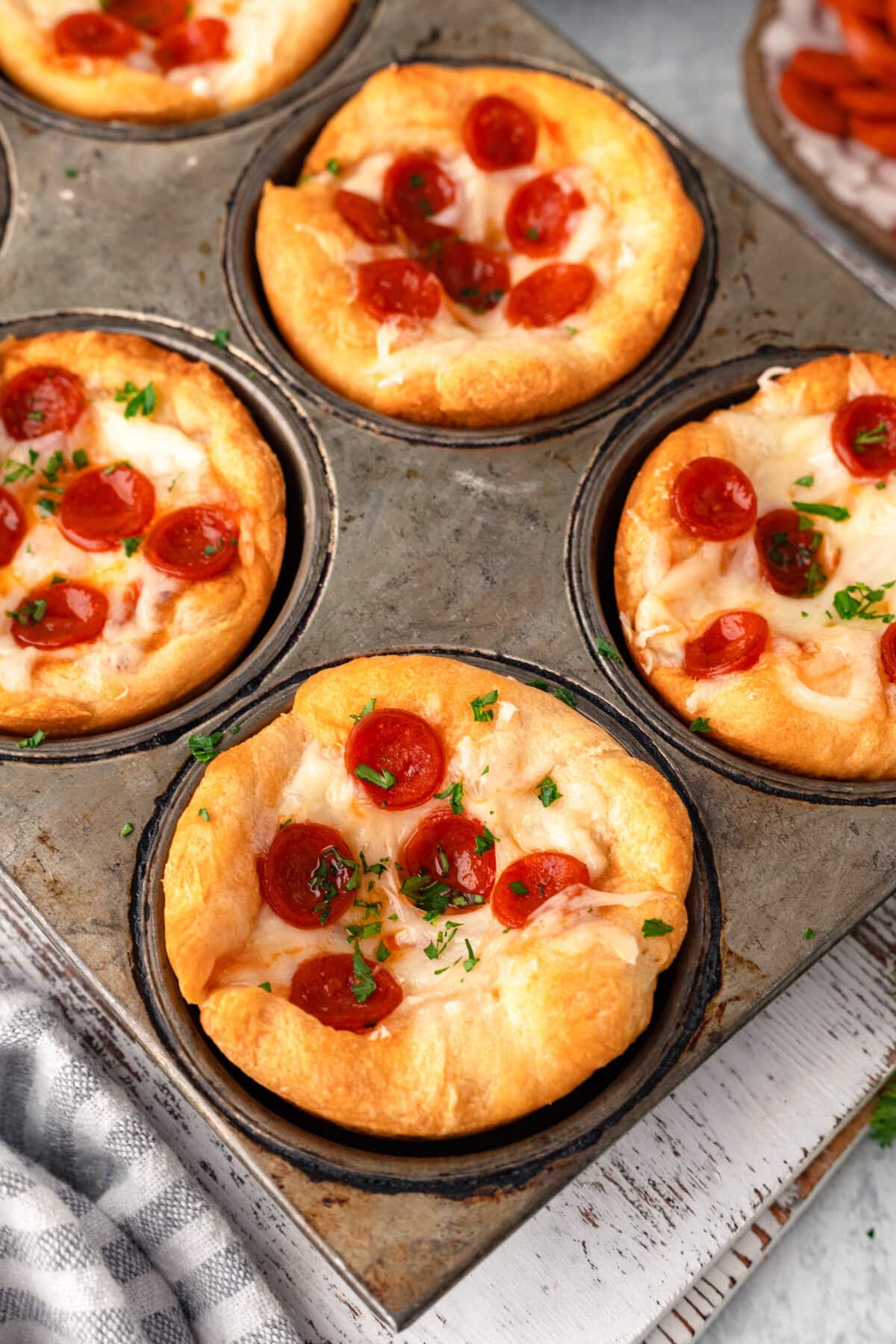 Mini pepperoni pizzas in muffin tins, fresh baked, cheesy, and garnished with parsley.